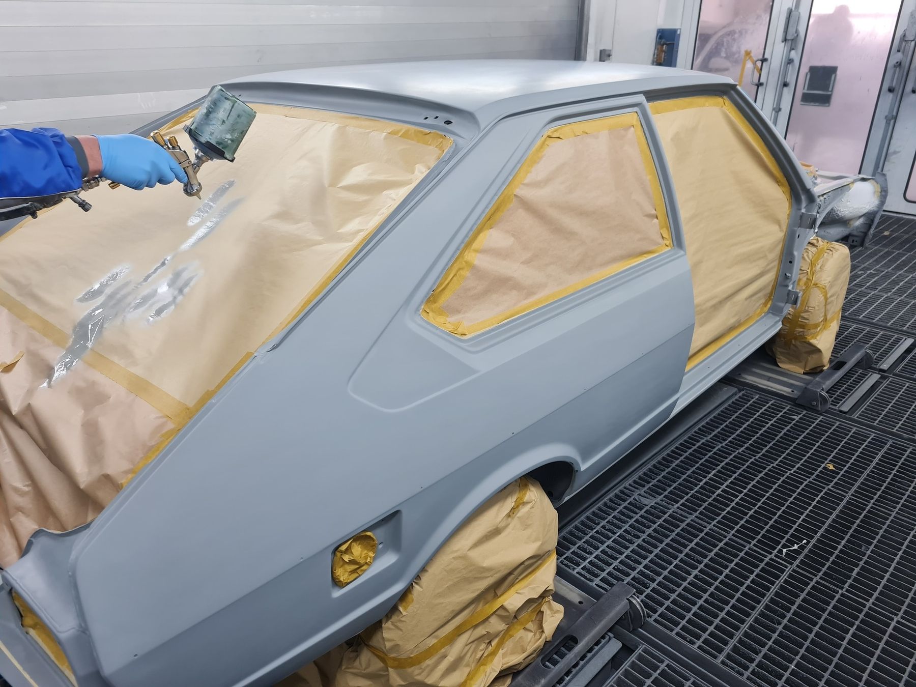 Ein Lackierer in Arbeitskleidung lackiert ein VW Passat in grau